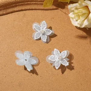 Tre fiori bianchi in pizzo e tulle con centri di perla sono disposti su una superficie color cuoio