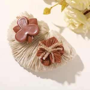 Two brown flower accessories, one smooth and one adorned with sparkling beads, on a cream display.