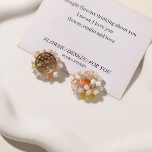 Close-up of two woven bead ornaments in cream, orange, pink and yellow on a white ceramic tray