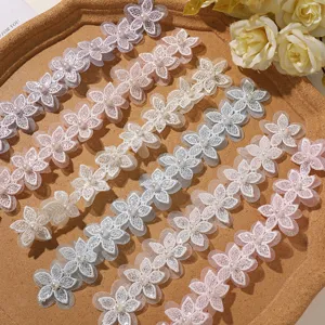 Fiori in pizzo con perla al centro, in bianco, rosa, beige e grigio, disposti su vassoio di legno
