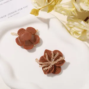 Two brown sculpted flower accessories with clear bead accents, arranged on a white ceramic dish