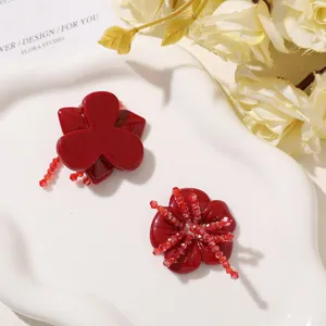 Two red flower hair clips on a white dish, one accented with sparkling red crystal beads