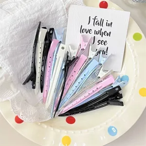 Close-up of assorted pastel and black duckbill hair clips arranged on a dotted ceramic plate
