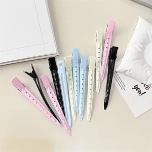 Pastel hair clips in pink, black, blue and ivory, with perforated bodies, arranged on a light surface