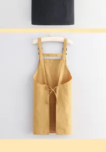 Gele schort aan een hanger, met schouderbanden, een geknoopte tailleband en licht gekreukte stof.