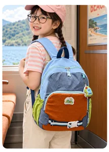 Enfant portant un sac à dos coloré, avec boucle frontale et pendentif, près d’une fenêtre de train
