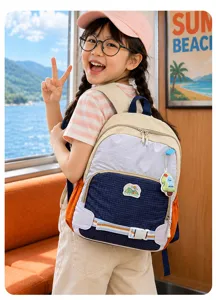 Enfant avec sac à dos beige et bleu marine, panneau quadrillé et breloque colorée près de la mer