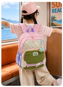 Vue de dos d’un enfant portant un sac à dos rose color-block, avec poche verte et breloque dinosaure