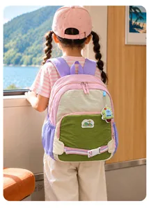 Vue de dos d’un enfant portant un sac à dos rose, vert et violet près d’une fenêtre donnant sur un lac