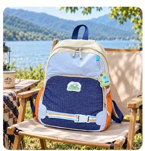 Vue du sac à dos à carreaux avec écusson camping et breloque dinosaure près d'un lac