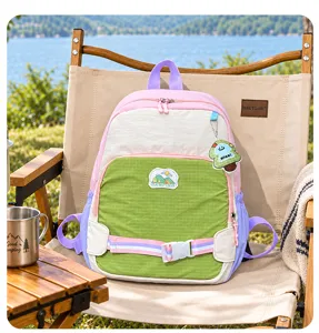 Sac à dos coloré avec poche avant verte et breloque, posé sur une chaise beige près du lac