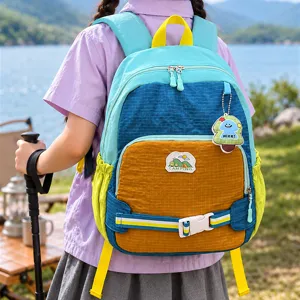Sac à dos enfant de plein air, turquoise, bleu et orange, porté par un modèle au bord d’un lac