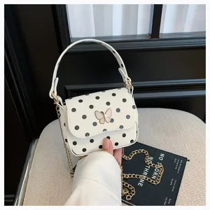 Gros plan sur un sac blanc à pois, avec fermoir papillon et chaîne dorée, tenu à la main