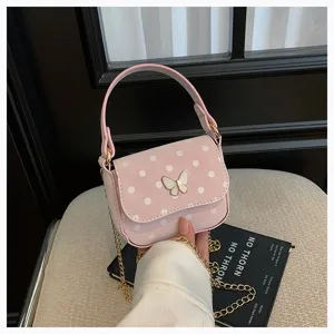 Détail d’un sac rose à pois, avec fermoir papillon et chaîne dorée, tenu devant un fauteuil