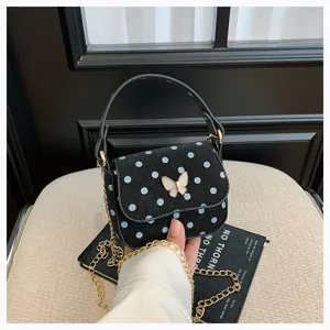 Détail d’un sac noir à pois blancs, avec fermoir papillon, poignée et chaîne dorée