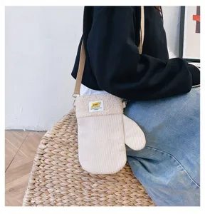 Gros plan sur un sac ivoire en velours côtelé, en forme de moufle, porté en bandoulière.