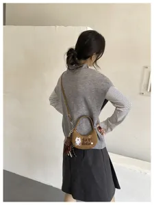Vue de dos d’un modèle portant un sac demi-lune brun en suédine, avec broderie d’ours et peluche