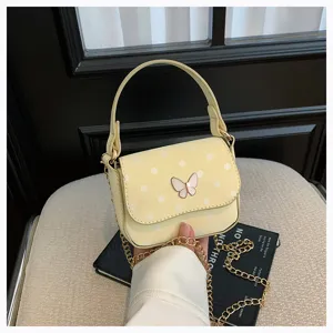 Gros plan sur le sac jaune pâle à pois, avec fermoir papillon et chaîne dorée, tenu à la main