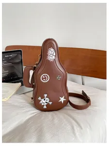 Sac guitare marron en similicuir, avec écussons brodés et ferrures dorées, posé sur un lit