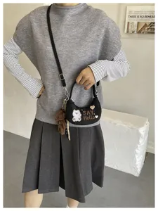 Une personne porte un petit sac noir demi-lune, avec un ours blanc imprimé et un pendentif ours brun