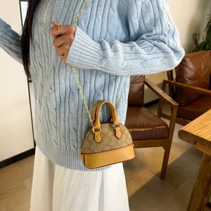 Petit sac à monogramme brun, bordure camel et chaîne dorée porté à l’épaule en intérieur