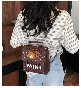 Vue de dos d’une personne portant un mini sac à dos brun à pois blancs, avec un ourson et un nœud