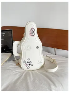 Détail des broderies, des éléments dorés et de la bandoulière d'un sac blanc en forme de guitare