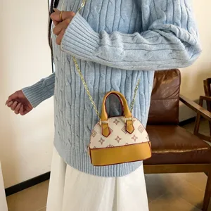 Petit sac crème à motif, bord caramel et chaîne dorée, porté par un mannequin en intérieur