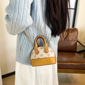 Une personne porte un petit sac coquillage ivoire à motif, bordure caramel et chaîne dorée
