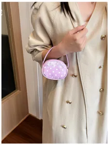 Une main porte un petit sac rond violet à pois blancs, avec bordure en dentelle et fermeture éclair.