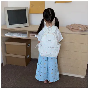 Vue de dos d’un enfant portant un sac blanc à étoiles colorées, debout devant un bureau