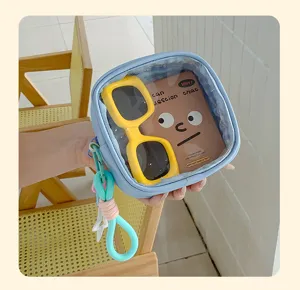 Gros plan sur une trousse transparente à bord bleu, avec lunettes jaunes et dragonne colorée