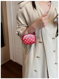 Un petit sac rouge à pois et bordure en dentelle blanche est tenu devant un manteau beige
