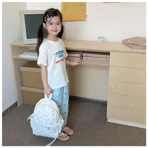 Une fille présente un sac à dos bleu clair imprimé, avec un tee-shirt blanc et un pantalon assorti