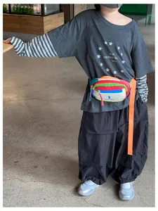 Enfant portant un tee-shirt gris, des manches rayées, un pantalon large et un sac banane coloré