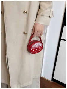 Une main tient un petit sac rond rouge à pois blancs, avec dentelle et fermeture zippée