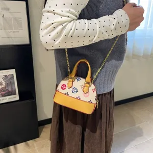 Vue portée d’un petit sac crème à motifs colorés, bordure jaune et bandoulière chaîne dorée.