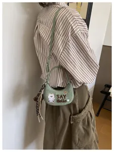 Sac vert effet daim porté en bandoulière, brodé d’un ours, avec « SAY Hello » et pompon tressé.