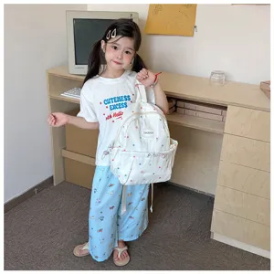 Un enfant présente à l’intérieur un sac à dos blanc à étoiles colorées devant un bureau en bois