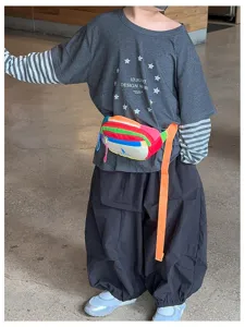 Enfant portant une banane multicolore sur un haut gris, avec un pantalon sombre et ample