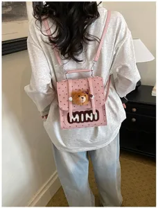 Vue de dos d’un modèle portant un petit sac rose à pois, avec un pendentif ourson et l’inscription MINI