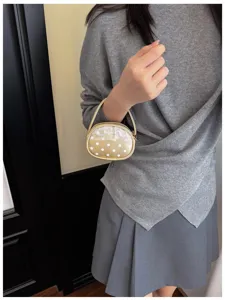 Petit sac ovale bordé de doré, à pois blancs et dentelle, porté avec une tenue grise