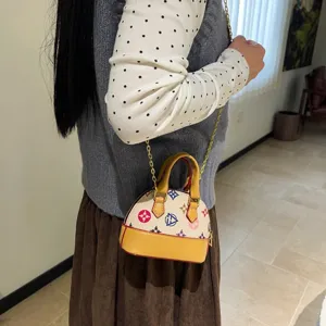Petit sac coquillage crème porté en bandoulière, avec motifs colorés, bordure jaune et chaîne dorée