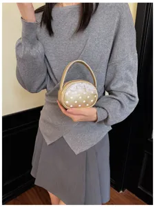 Gros plan sur un mini sac rond doré à pois blancs, avec bordure en dentelle et anse courbe