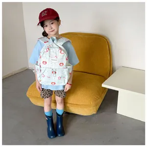 Enfant portant un sac à dos bleu clair à motifs de pommes et carreaux près d’un canapé moutarde