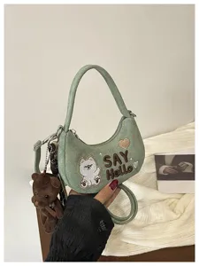 Détail d’un sac vert avec chien brodé, cœur, inscription « SAY Hello » et breloque ourson
