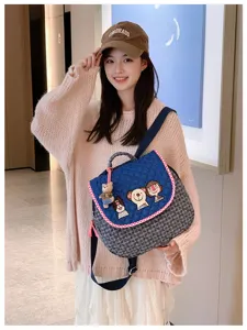 Sac matelassé bleu porté, bord à carreaux rouges, écussons illustrés et petit charm ourson