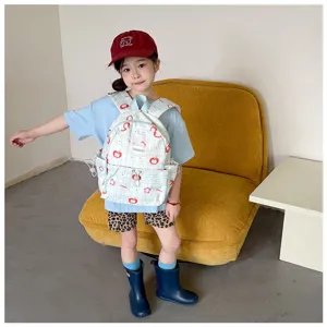 Un enfant porte un sac à dos à carreaux bleu clair, décoré de pommes rouges, devant un canapé jaune.