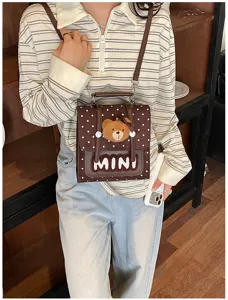 Détail d’un petit sac bandoulière brun à pois, avec un ours en peluche et l’inscription MINI