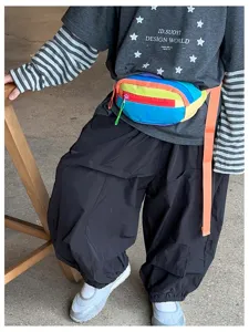 Gros plan sur un enfant avec sac banane arc-en-ciel et sangle orange, porté sur un pantalon noir